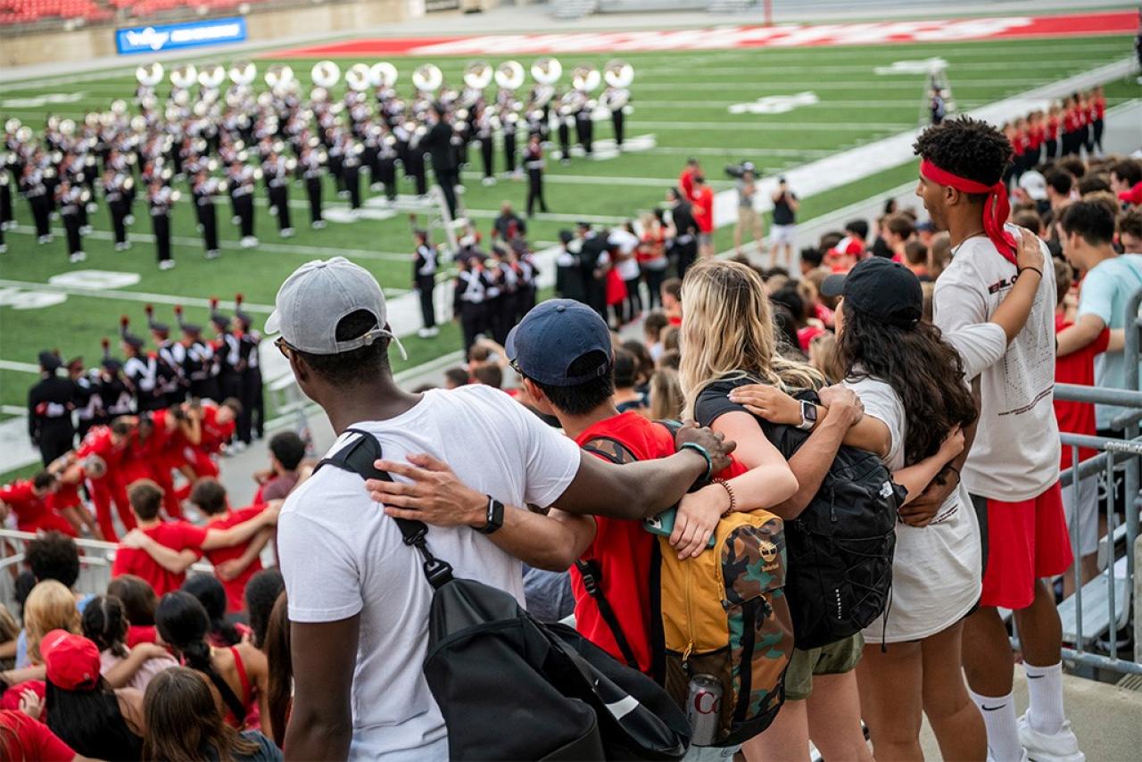 Students singing Carmen Ohio in the stadium while the marching band plays in formation on the field