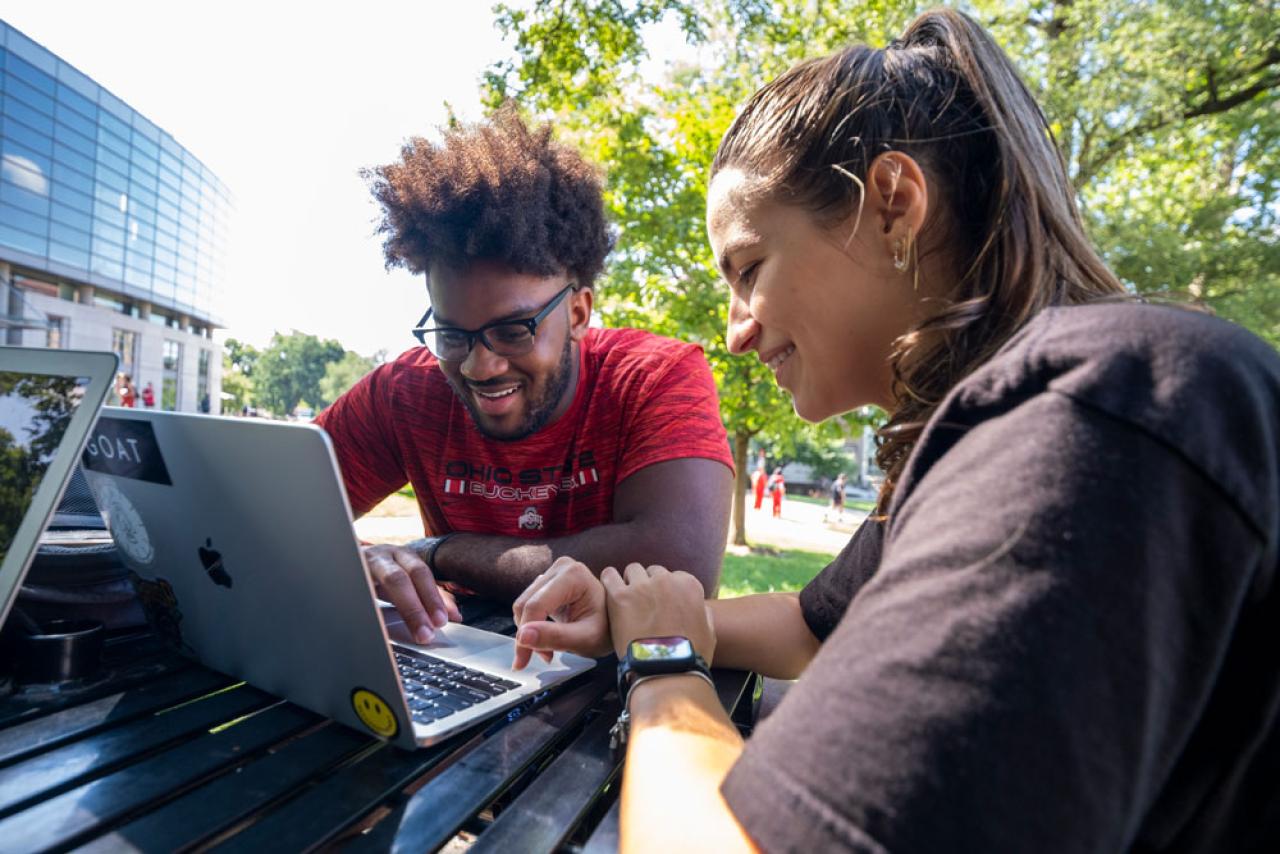 Two Ohio State students looking at something on a computer screen while sitting outside