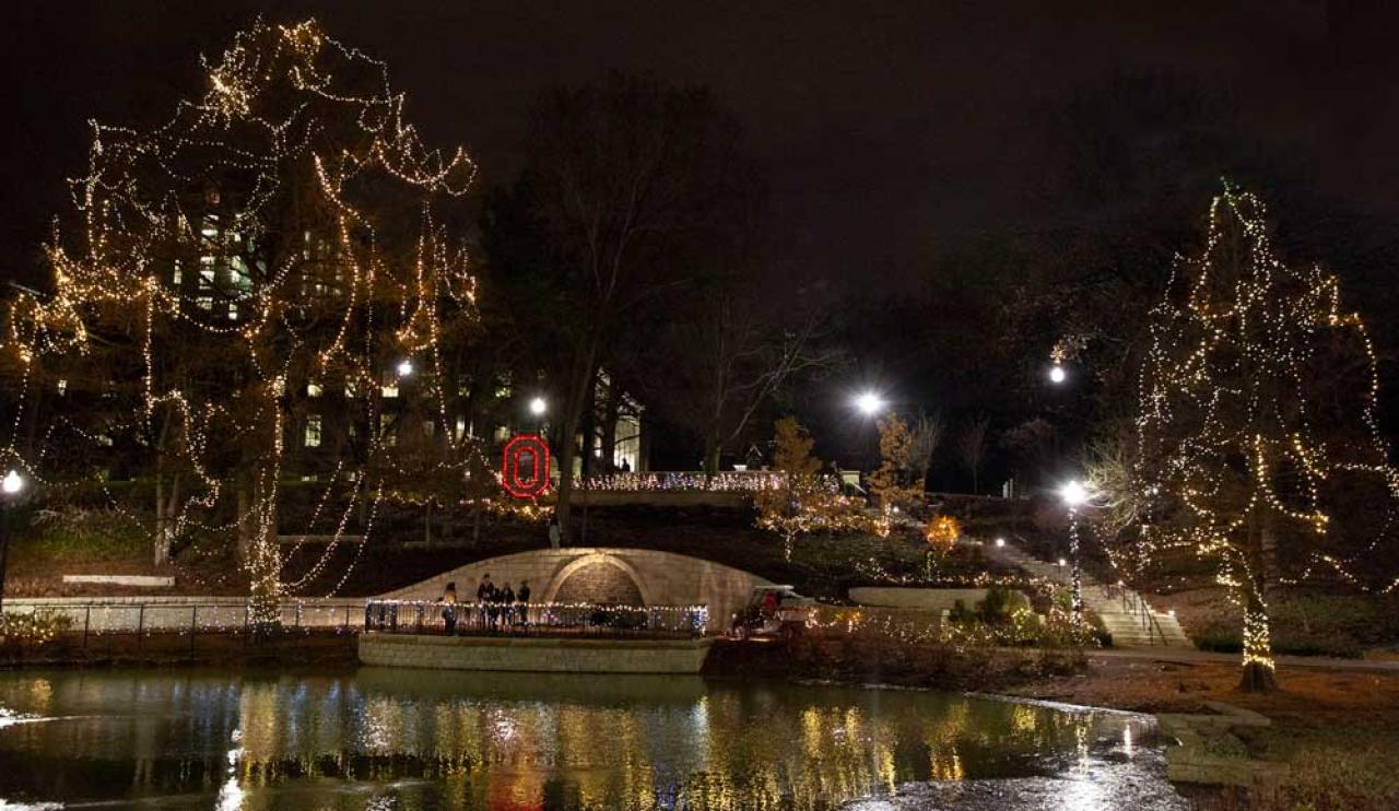 Trees surrounding Mirror Lake decorated with clear holiday lights. A block O made of red holiday lights is positioned at center.