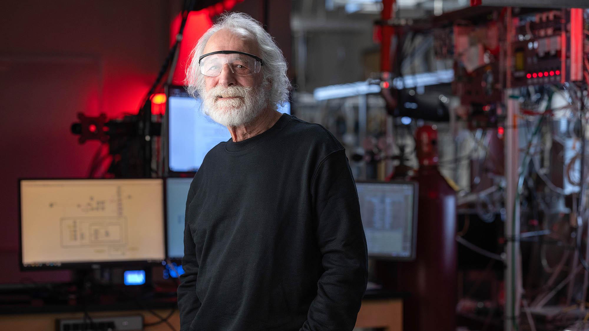 Pierre Agostini in a black shirt and lab eye protection in front of various machines during one of his visits to OSU campus.