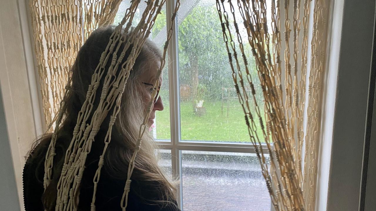 Woman looking through window curtains to view flooding outside